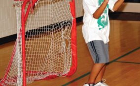 A young boy wearing a white t-shirt and shorts playing as a goalie in front of a small indoor net.