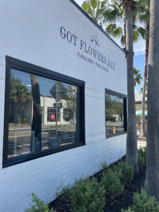 Exterior of "Got Flowers Jax" floral shop with two large windows and palm trees in front.