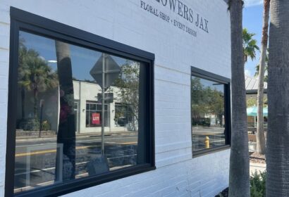 Exterior of "Got Flowers Jax" floral shop with two large windows and palm trees in front.