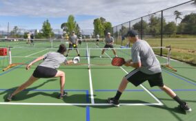 Four people playing pickleball on an outdoor court, with two teams engaged in a rally.