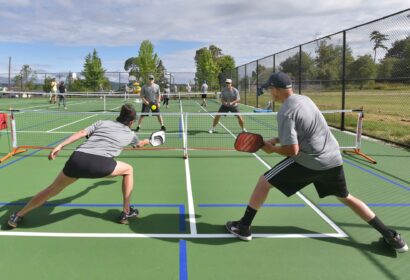 Four people playing pickleball on an outdoor court, with two teams engaged in a rally.