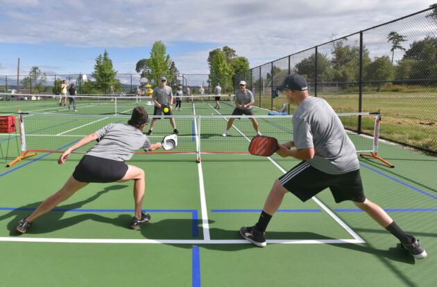 Four people playing pickleball on an outdoor court, with two teams engaged in a rally.