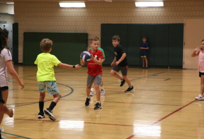 Children playing basketball in a gymnasium, with one boy holding a ball and others moving around the court.