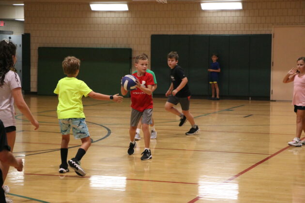 Children playing basketball in a gymnasium, with one boy holding a ball and others moving around the court.