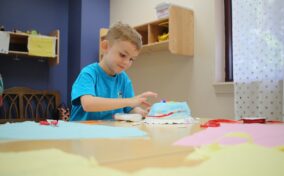 Child in a blue shirt crafting at a table, with colorful paper and scissors around.