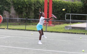 A young girl in athletic wear plays tennis on an outdoor court, hitting a ball with her racket.