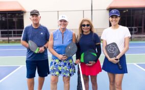 Four people stand on a pickleball court, each holding a paddle.