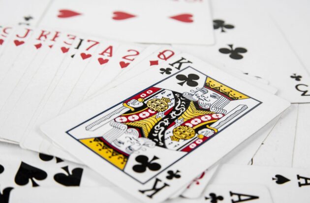 A deck of playing cards scattered on a surface, with the King of Clubs prominently visible in the center.