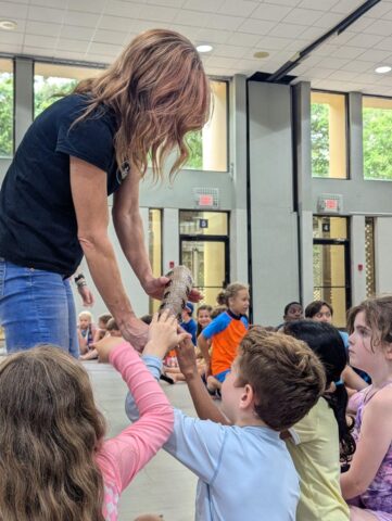 A woman holds a snake for children to touch in a classroom setting.