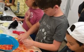 Children cutting vegetables together at a kitchen counter.