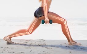 A person performs a lunge on a beach while holding dumbbells. Superimposed skeletal imagery shows bones in the arms and legs.