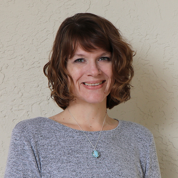 A woman wearing a gray sweater and a necklace.