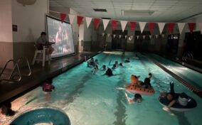 A group of youth floating in an indoor pool watching a movie.