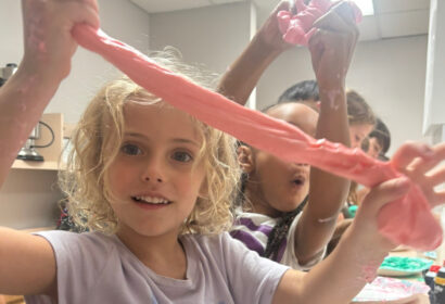 Children playing with pink slime in a room, stretching the slime between their hands and appearing engaged with the activity.
