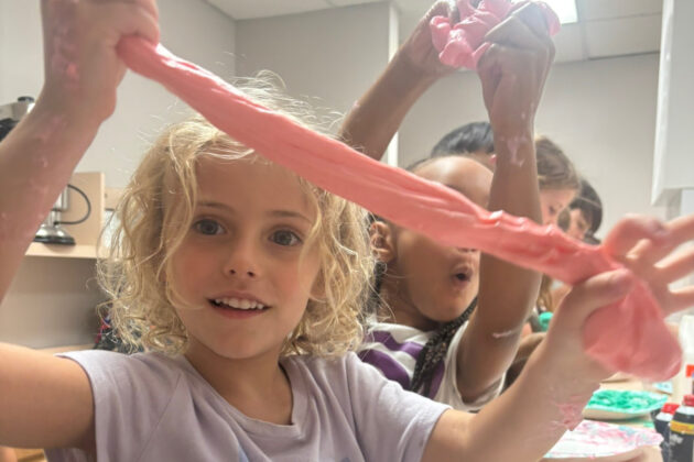 Children playing with pink slime in a room, stretching the slime between their hands and appearing engaged with the activity.