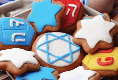 Assorted Hanukkah-themed cookies decorated with Stars of David and dreidels featuring Hebrew letters, arranged on a plate.