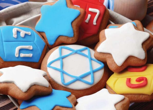 Assorted Hanukkah-themed cookies decorated with Stars of David and dreidels featuring Hebrew letters, arranged on a plate.