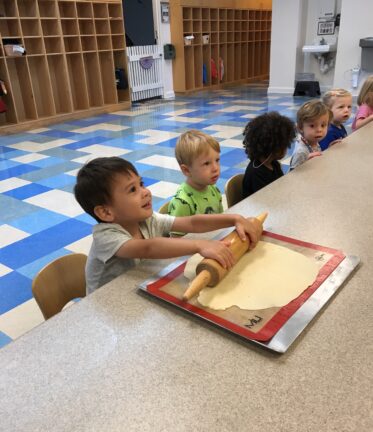 A group of children sitting at a table with a rolling pin.