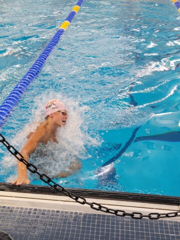 A swimmer in a pink swim cap touches the pool wall at the end of a race, creating a splash of water.