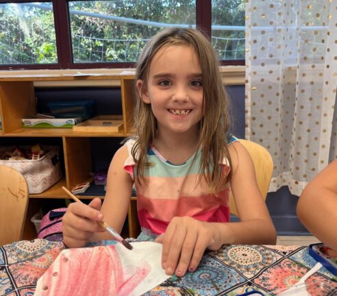Girl smiling with paintbrush in hand as she paints.