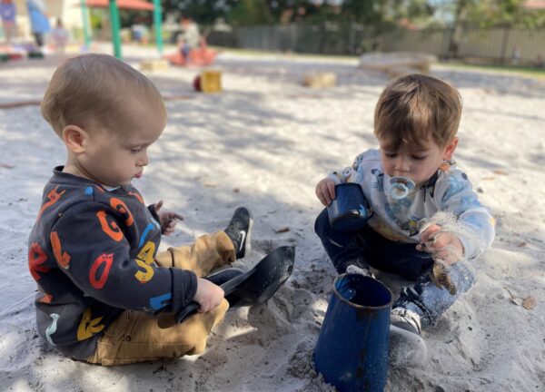 Two toddlers playing in the sand at a playground.