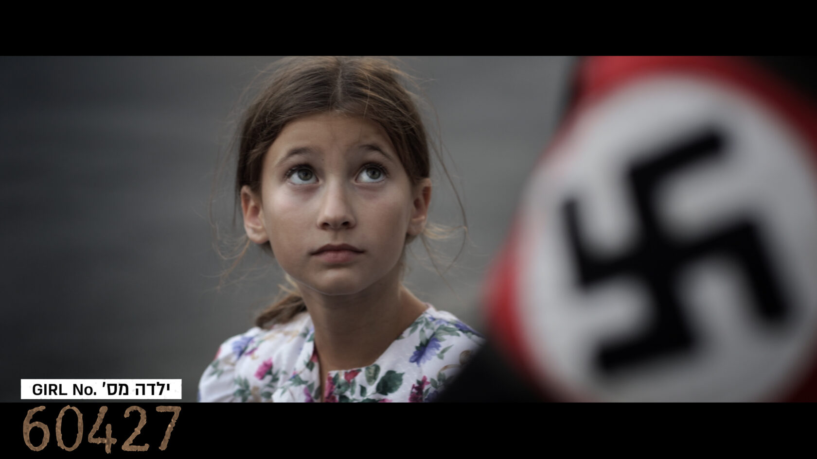 A young girl with a floral dress looks upward, with a blurred swastika flag in the foreground and the number 60427 in the corner.