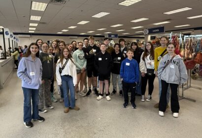 A group of people wearing casual clothing pose for a photo inside a store. Name tags are visible on their clothing, and store signs are in the background.