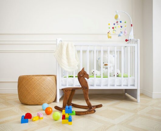 White crib with toys and mobile in nursery. Wooden rocking horse, balls, and building blocks on the floor. Beige woven basket nearby.