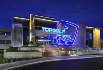 Exterior of a Topgolf venue at night, featuring bright neon signage and lit entrance stairs.