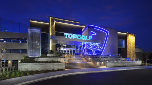 Exterior of a Topgolf venue at night, featuring bright neon signage and lit entrance stairs.