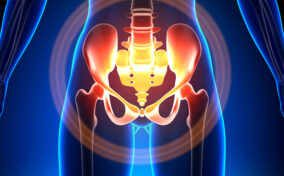 Digital illustration showing the lower torso and pelvis with a focus on the hip joints and pelvic bones, highlighted in red and orange to indicate pain or inflammation.