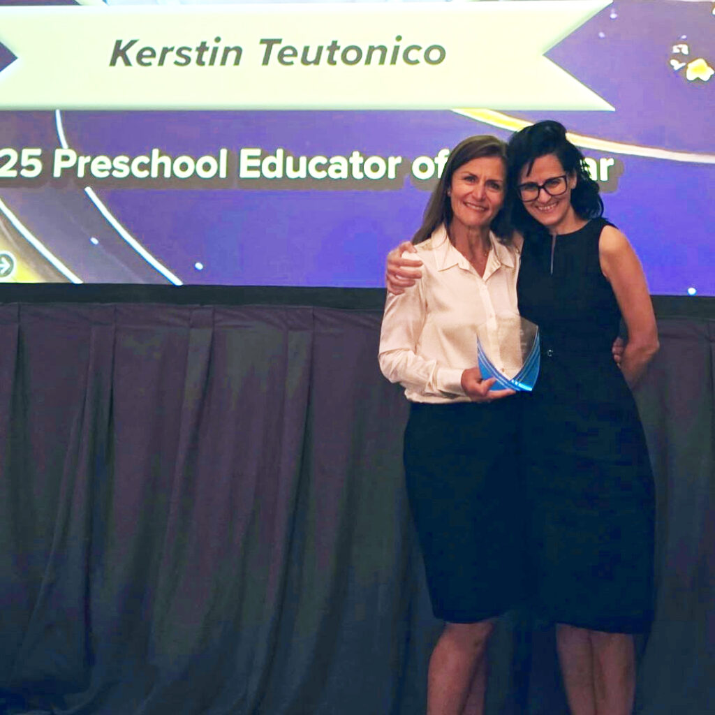 Two women stand together smiling on stage; one holds an award. A screen behind them reads "Kerstin Teutonico 2025 Preschool Educator of the Year.