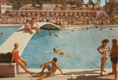 People relax, swim, and sunbathe around a crowded outdoor pool at a resort; lounge chairs, umbrellas, and a bridge are visible.