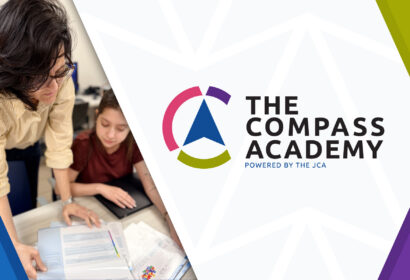 A woman helps a student with paperwork at a table. At right, The Compass Academy logo and text "Powered by the JCA" are displayed on a geometric background.