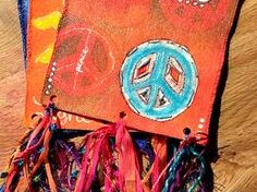 Two handmade fabric banners, one with the word "Peace," peace symbols, and colorful ribbon tassels, lying on a wooden surface.