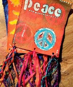 Two handmade fabric banners, one with the word "Peace," peace symbols, and colorful ribbon tassels, lying on a wooden surface.