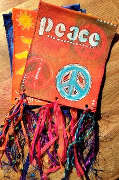 Two handmade fabric banners, one with the word "Peace," peace symbols, and colorful ribbon tassels, lying on a wooden surface.