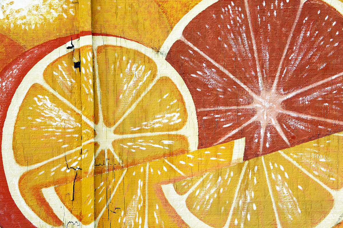 Close-up of a painted mural showing a yellow lemon slice and a red grapefruit slice on a textured wooden surface.
