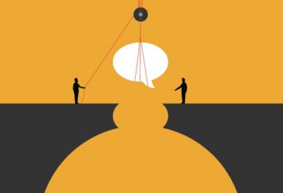 Two people stand on opposite sides of a gap, using ropes and a pulley to lift a large speech bubble between them, symbolizing communication or bridging a divide.