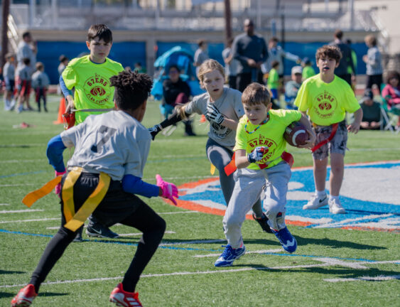 Youth flag football players in neon yellow and grey jerseys running on a field during a game.
