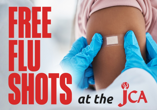 A medical professional in blue gloves places a bandage on a patient’s arm, with the text “FREE FLU SHOTS at the JCA.”